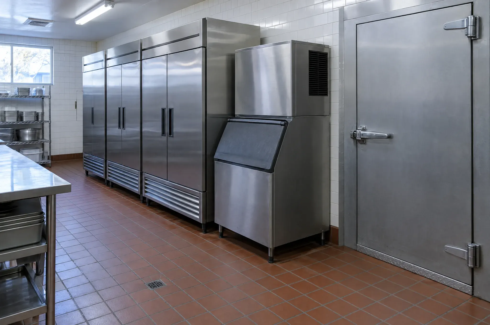 Stainless steel reach-in refrigerators, an ice machine and a walk-in cooler door in the back of a restaurant kitchen.
